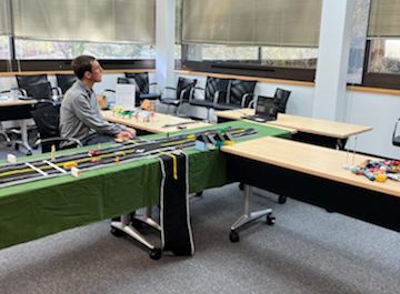 Image of Seth LaJeunesse sitting in front of a computer and beside a felt road with movable parts as he directs kids through a virtual road engineering demo.