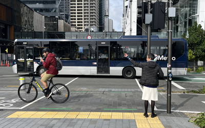A pedestrian waves to a cyclist while waiting at a crosswalk. Photo by Laura Sandt as part of FHWA's Global Benchmarking project trip to Australia and New Zealand.