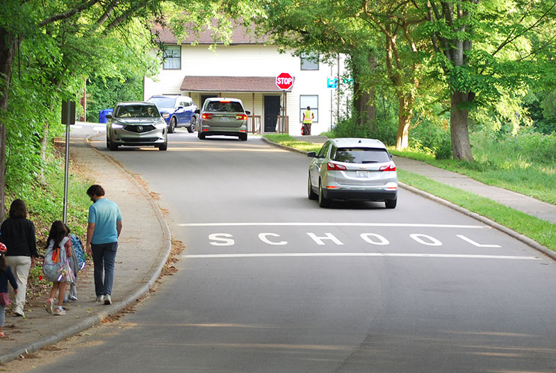 family walking on sidewalk next to a road with school zone painted on the concrete.