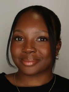 A headshot of a smiling person wearing a black shirt and a gold necklace.